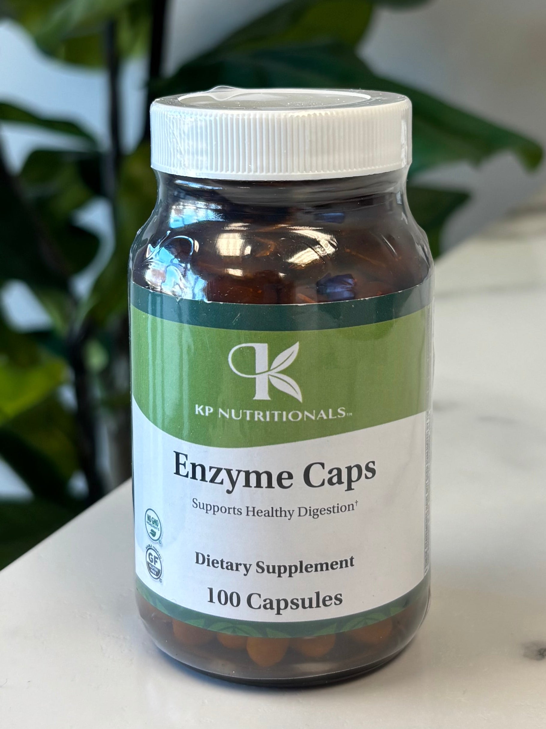 Supplement bottle labeled 'Enzyme Caps' on a marble surface with green leaves in the foreground